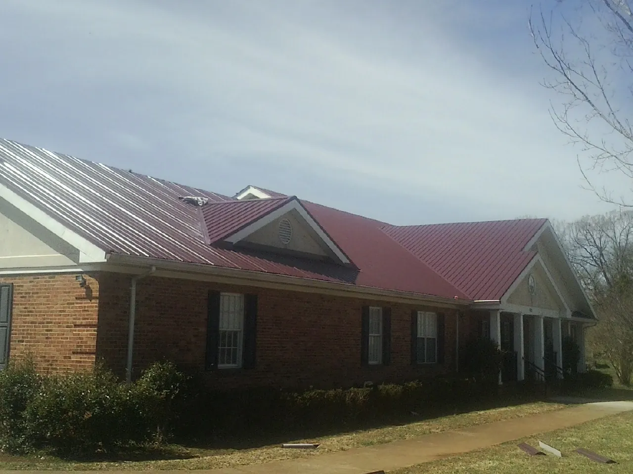 Red metal roof with gabled entries on a long brick building, from a Hail Damage Roof Repair job in Sloughhouse