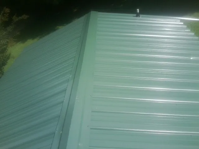 New green metal panels meeting at the ridge of a roof — Flat Roof Repair work by our crew in Sloughhouse