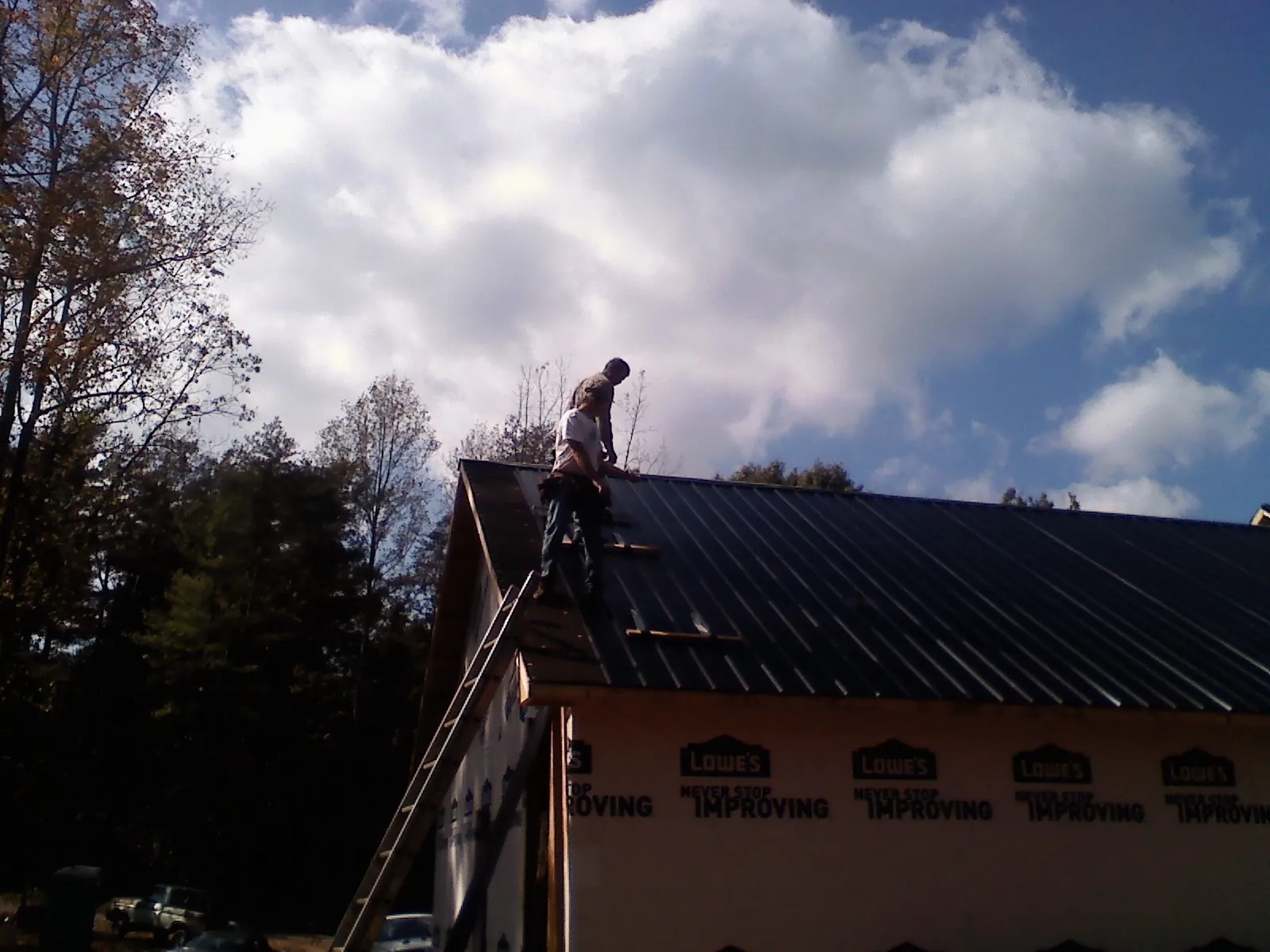 Roofer fastening dark metal panels high against a cloudy sky, from a Roof Inspection job in Sloughhouse