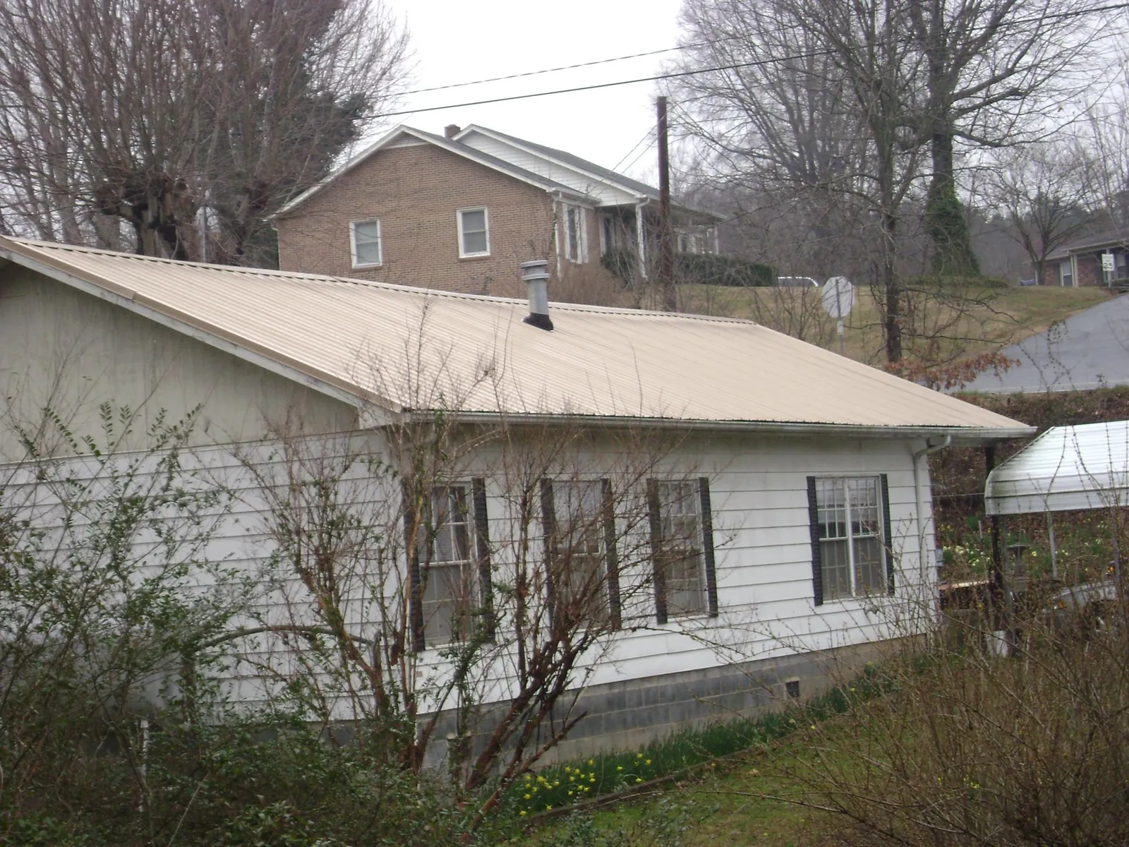 Tan metal roof on a white sided house set into a hillside — Commercial Roofing by Roofing Brothers in Sloughhouse